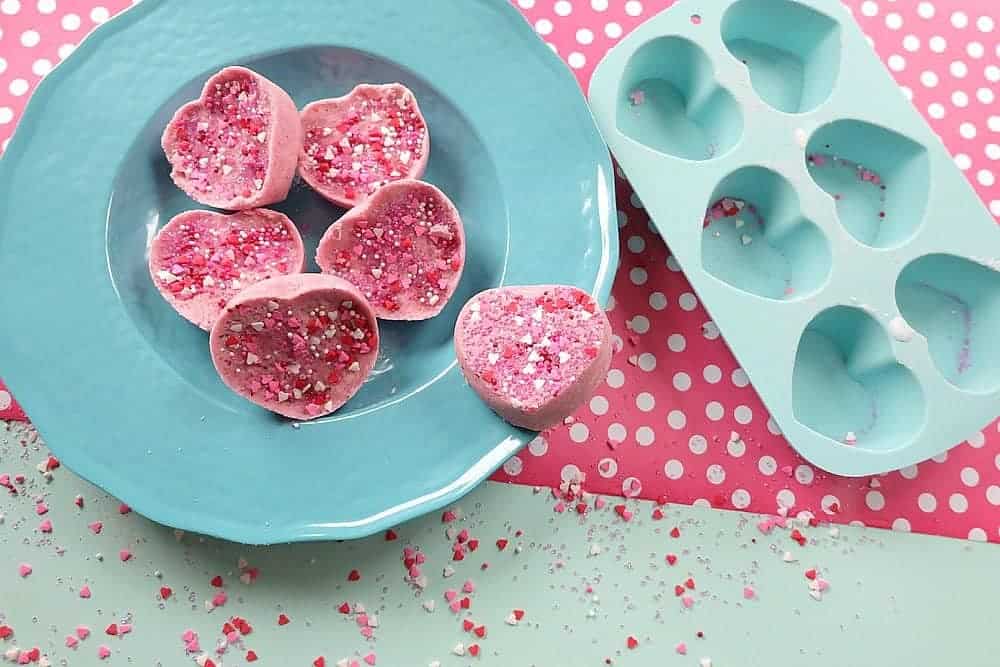 Heart bath bombs with pink sprinkles placed in a blue bowl