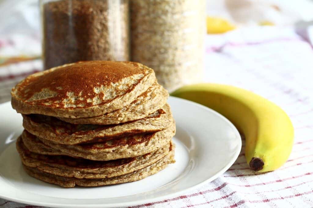 Stack of banana pancakes on a plate next to a banana