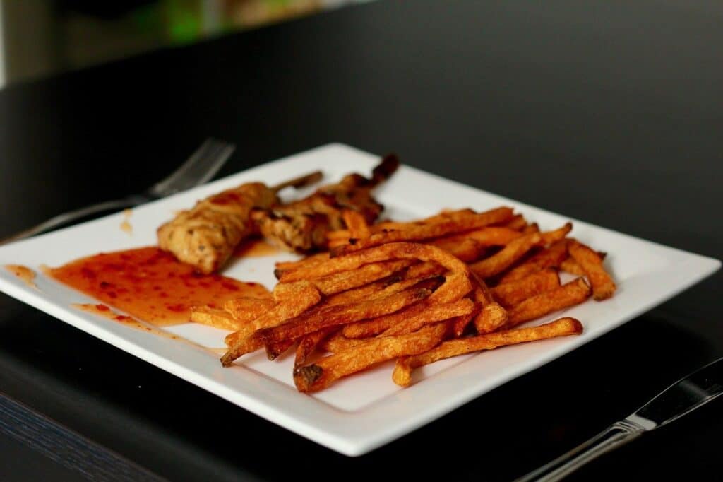 Sweet potato fries on a square plate with skewers and dipping sauce