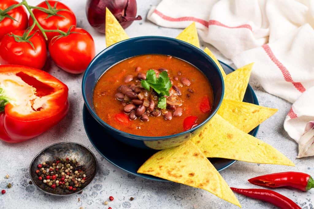 Tomato and kidney bean soup served with nachos and spices