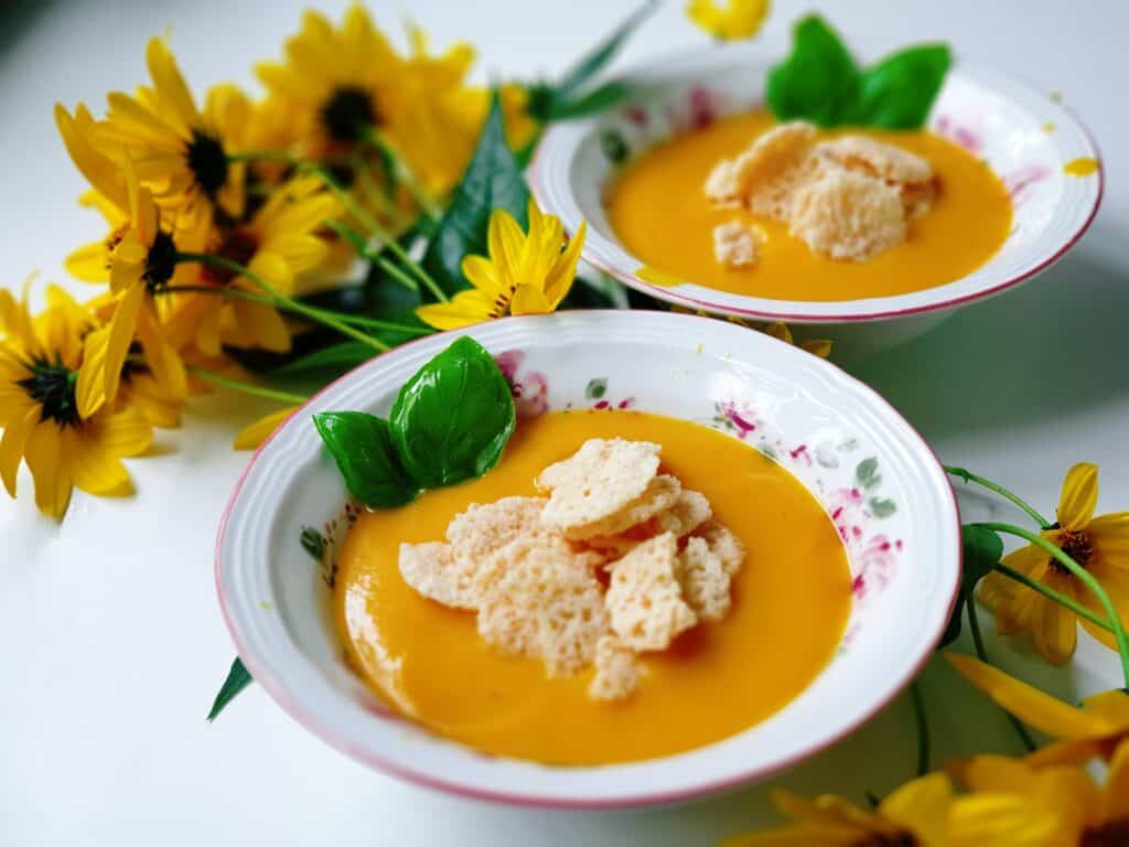 Pumpkin soup topped with croutons and basil with yellow flowers in background