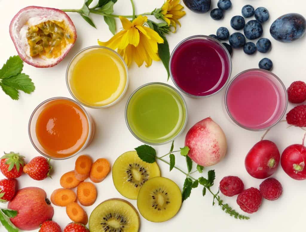 Series of different coloured smoothies in glasses surrounded by colourful fruit - breakfast alternatives to cereal