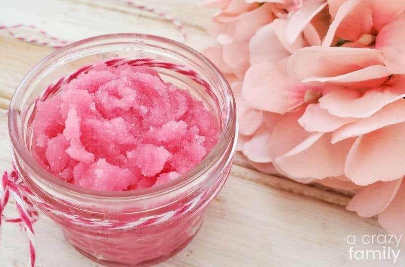 mango strawberry sugar scrub in a glass jar with a pink flower to side