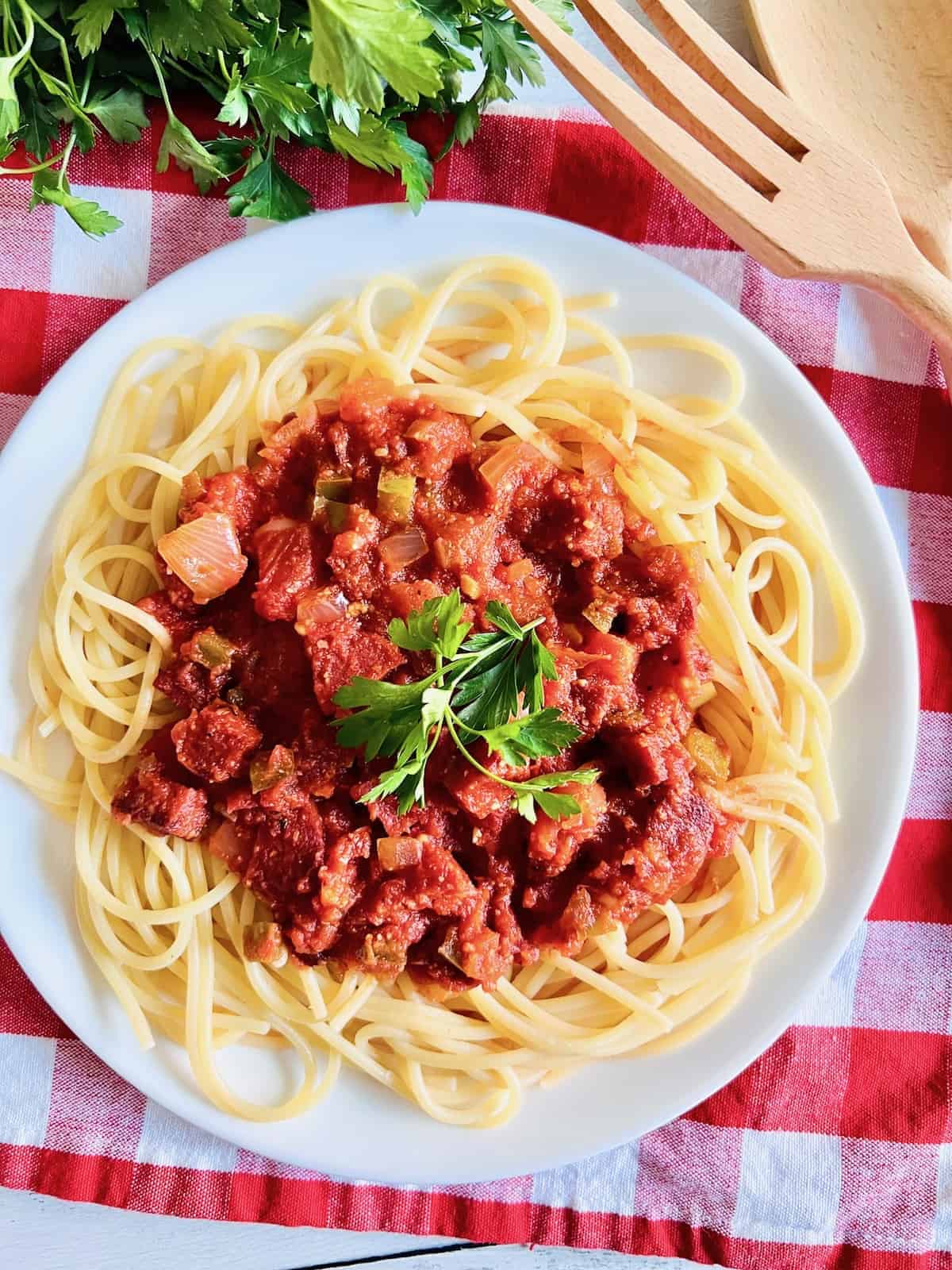 Pepperoni Spaghetti Overhead of plate with parsley surrounded by checked napkin parsley and serving utensils