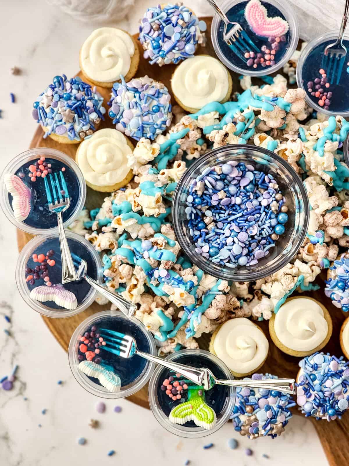 Little Mermaid Charcuterie Party Board with mermaid popcorn, Jello cups, and frosted cupcakes, perfect for a themed party or kids' celebration.