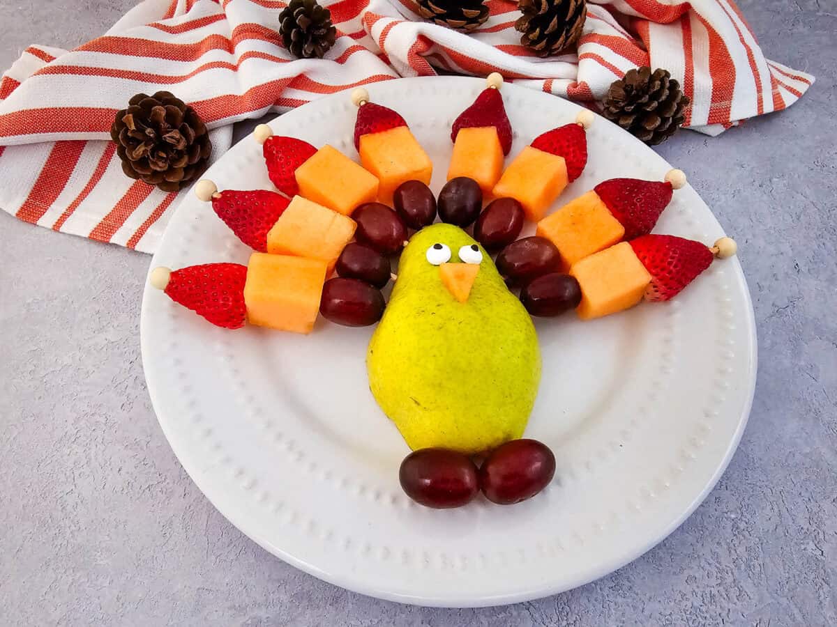 Thanksgiving turkey fruit skewers platter with pear body, strawberry, grape, and cantaloupe feathers.